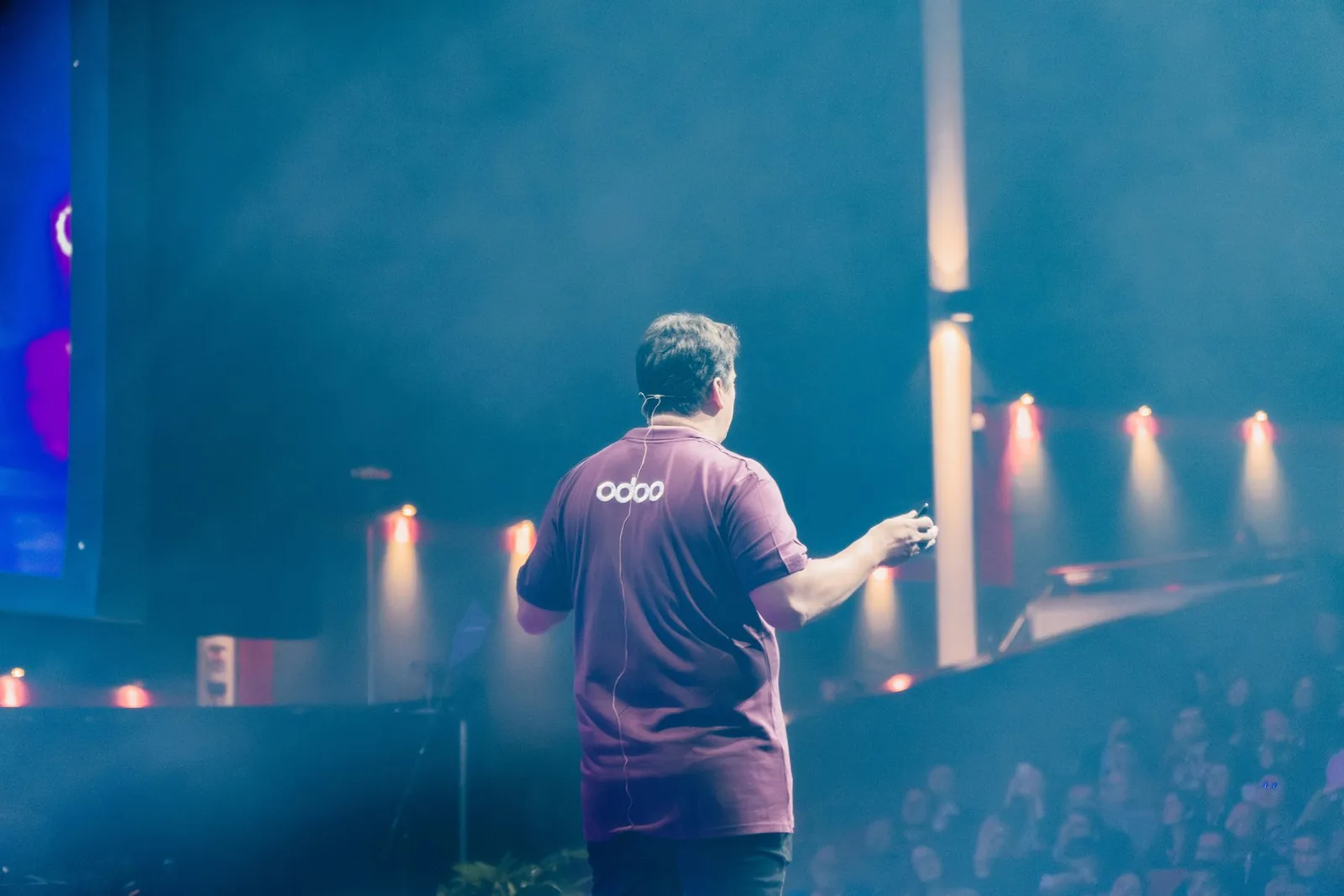 Доповідач у фірмовій футболці Odoo на сцені Odoo Experience перед залом зі слухачами